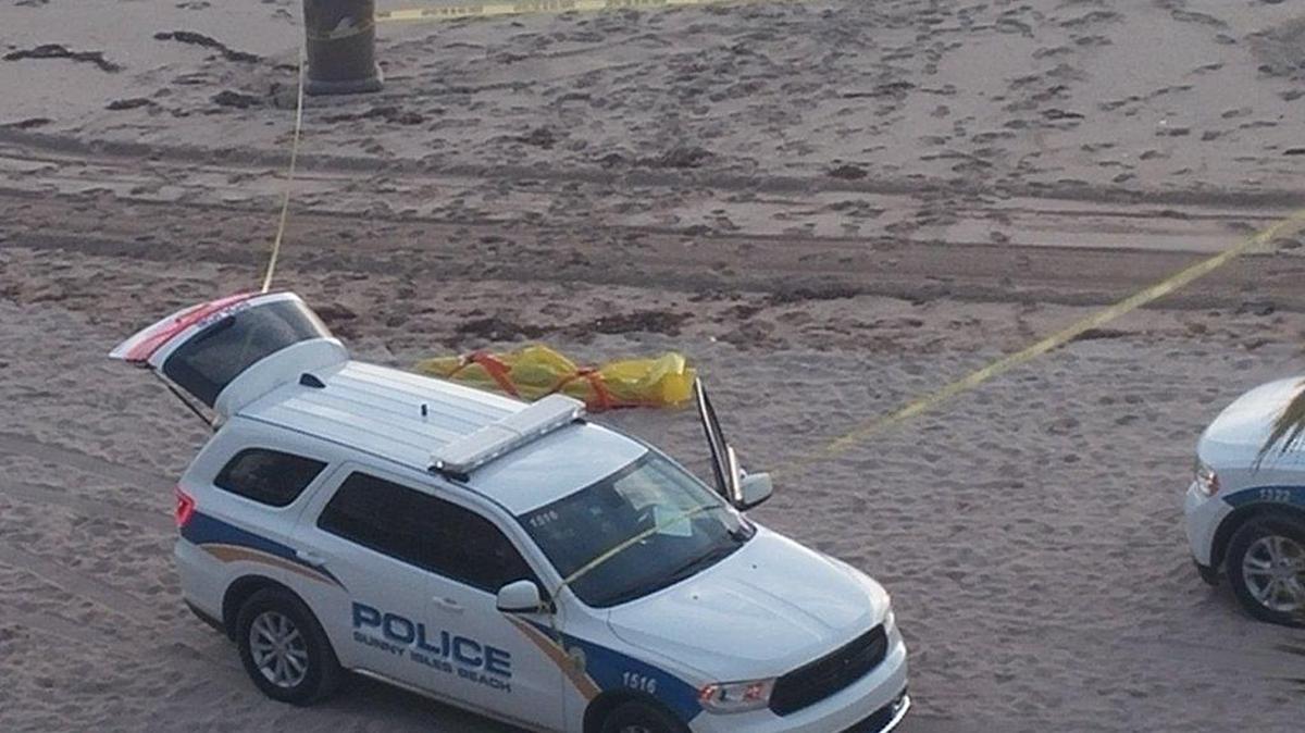 El cuerpo encontrado en las playas de Sunny Isles Beach, visto detrás de una de las camionetas de la policía local, el martes por la mañana.