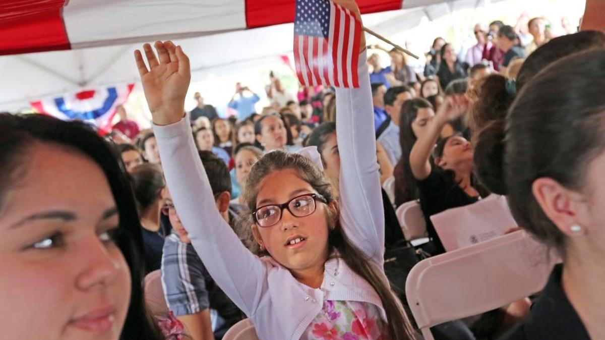 Janelle Vega, de ocho años de edad y nacida en Cuba, levanta los brazos para tocar la gigantesca bandera estadounidense sobre los 150 nuevos ciudadanos en una ceremonia en el Parque Nacional Biscayne.