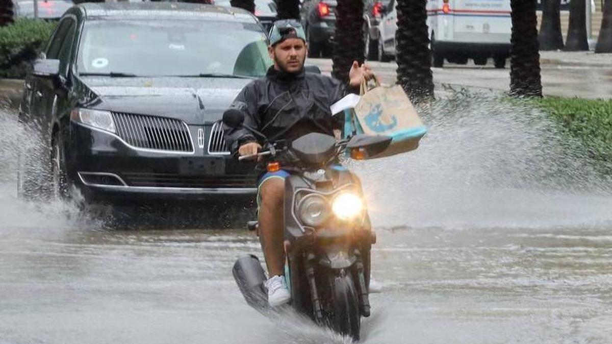 Un repartidor de comida en una motoneta avanza en medio de la calle inundada en Brickell este jueves.
