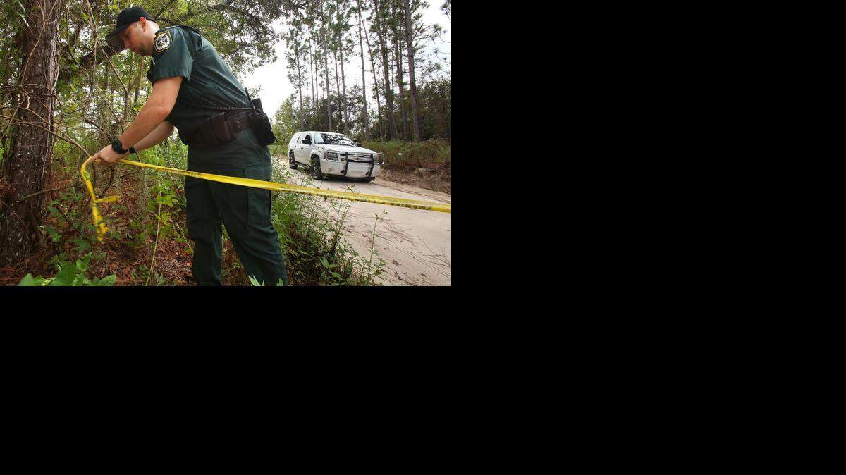 
El oficial del condado Gilchrist Robert Whitaker ata la cinta de la escena del crimen en el perímetro de la NW 29 Terrace, en Bell, Florida, el viernes 19 de septiembre de 2014. El jueves, un hombre mató a su hija y a sus seis nietos, y luego se suicidó.
