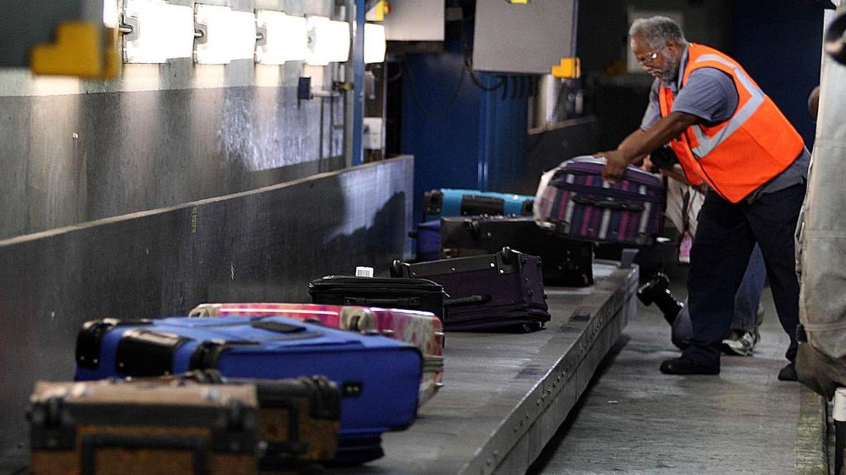 Un empleado del Aeropuerto Internacional de Miami (MIA) coloca piezas de equipaje en una cinta transportadora. Foto de archivo.
