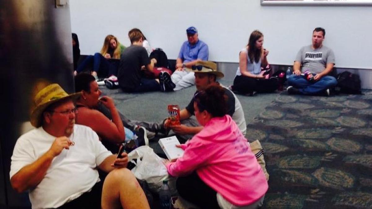 Los pasajeros retrasados en el aeropuerto de Fort Lauderdale esperan en el piso mientras empleados de Delta les entrega botellas de agua.