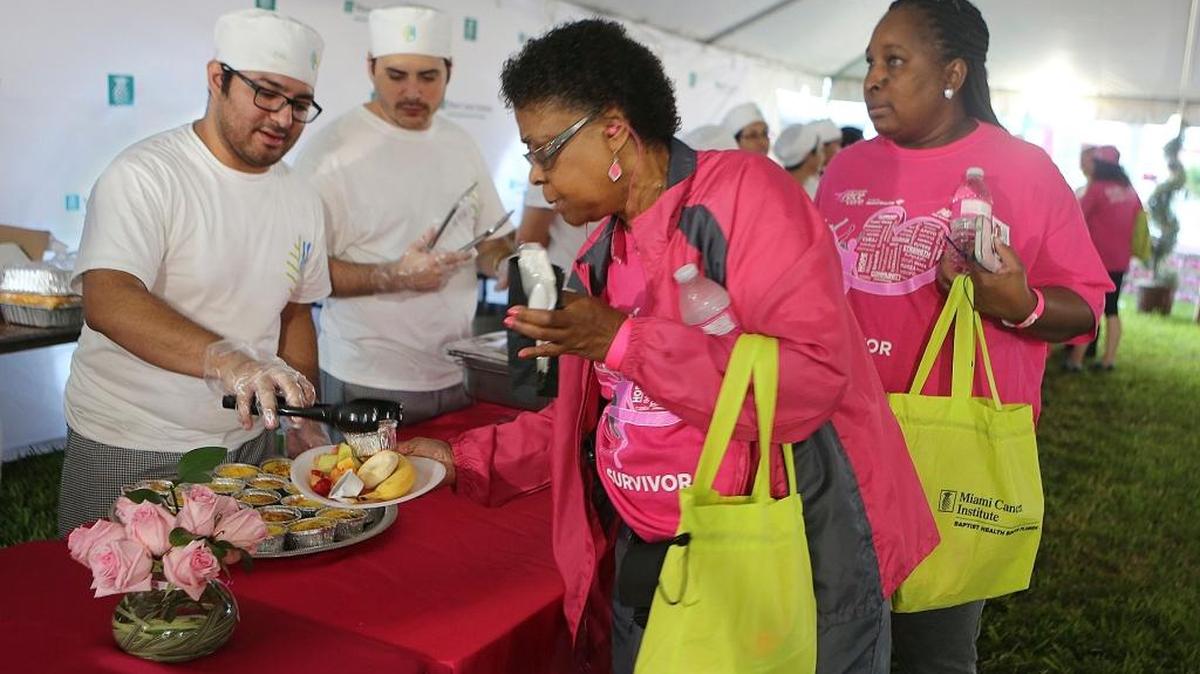 Los estudiantes William Espinoza (izq.), y Alberto Pereira sirven desayuno a Gale Rembert (centro) y Jessica Mobley en la Carpa de los Sobrevivientes antes de comenzar la carrera/caminata de 5K.