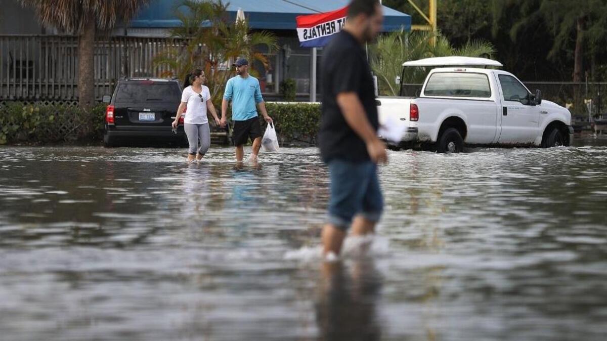 Yaneisy Dueñas y Fernando Sanudo caminan por un estacionamiento inundado en la marina de Haulover el 14 de noviembre.