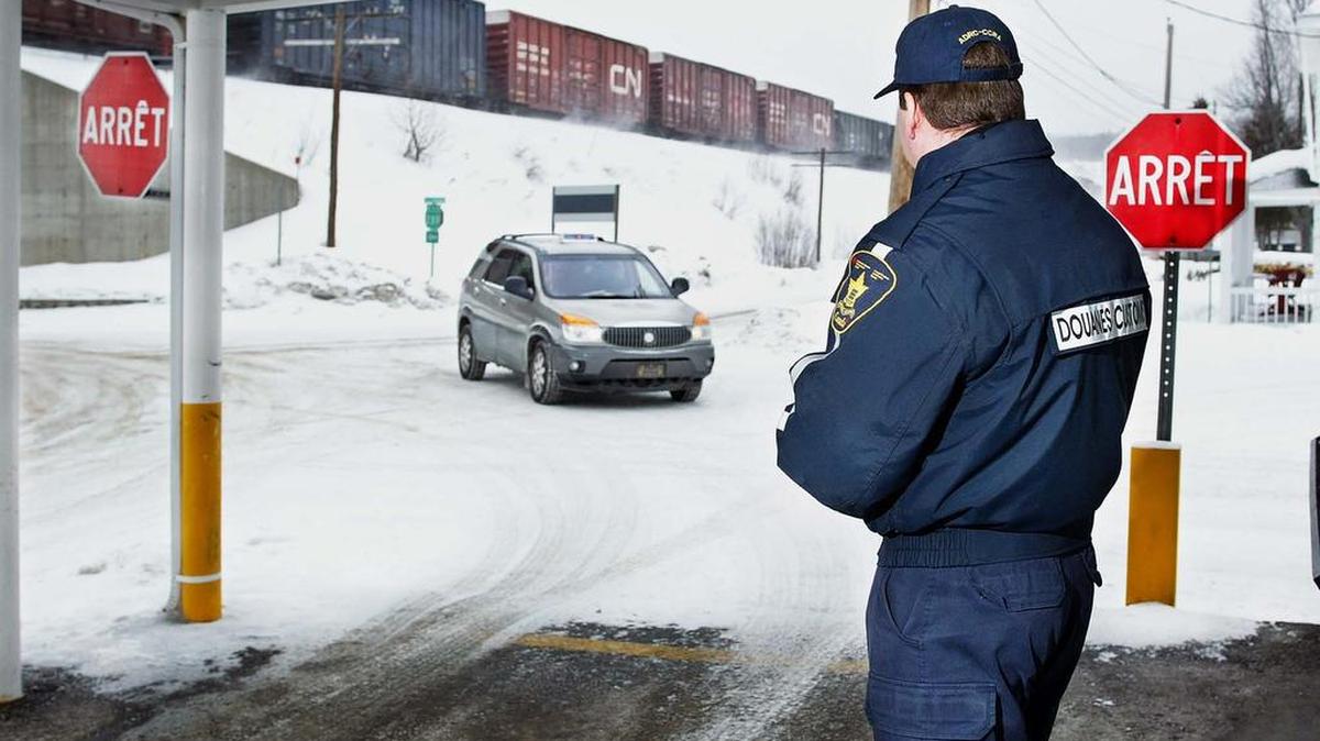 Un agente de aduanas canadiense observando a un vehículo en Pohenegamook, Quebec, a unos pocos metros de la frontera con Estados Unidos.