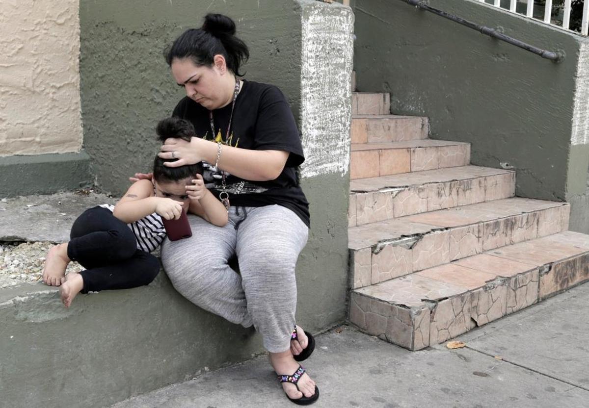 Taymara Linarte (derecha) arregla el cabello de su hija de tres años frente al edificio donde ella y sus cuatro hijos viven en 946 SW 4th St.