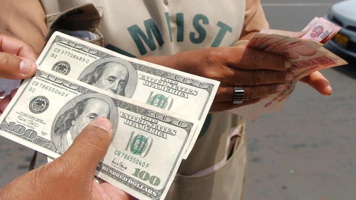 Una persona sostiene dos billetes de $100 mientras una cambista cuenta billetes peruanos en una calle de Lima, Perú. Ese país está considerado como un centro de falsificación de dólares.