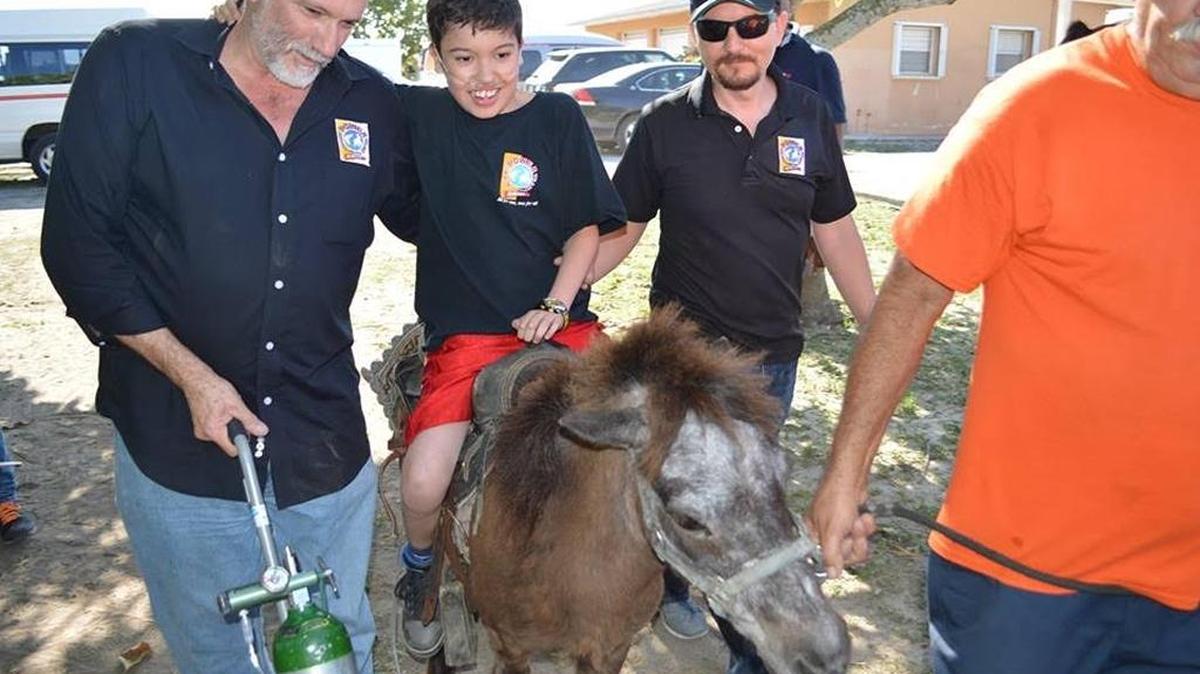 Alex Alcántara, aunque no puede mover completamente sus extremidades, logró por vez primera montar en un poni en su cumpleaños. Con Miguel Sánchez (izq.), presidente y fundador del Miami Power Team, y el voluntario John Sierra.