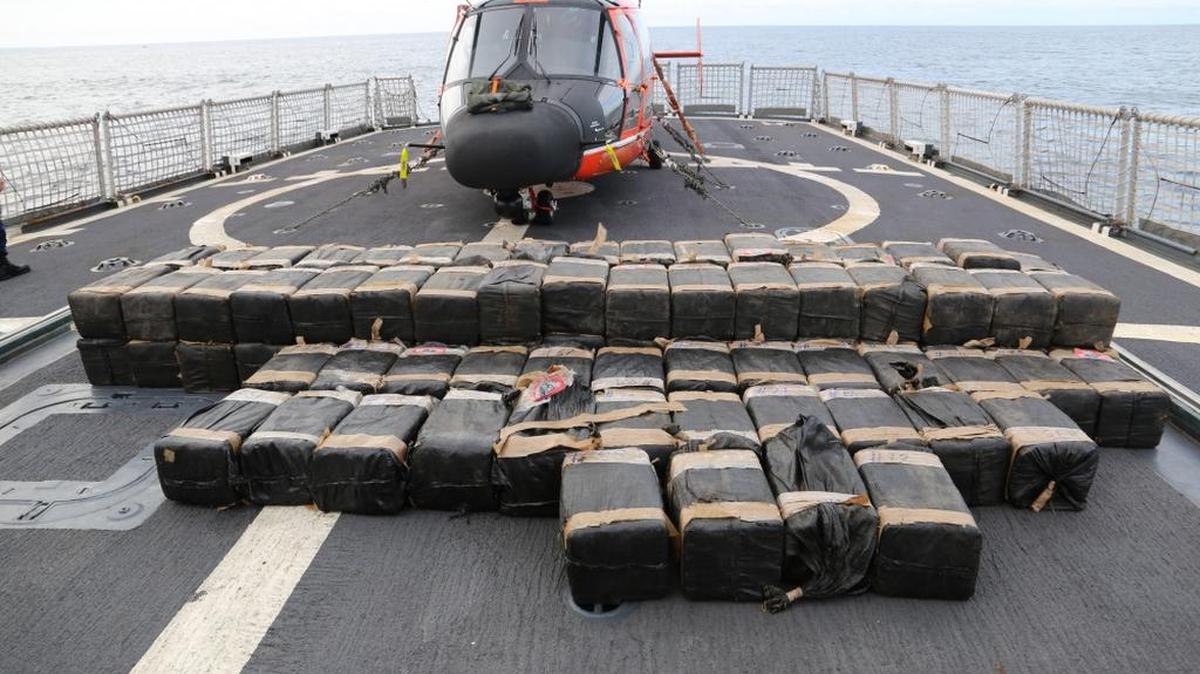 Más de 2,200 kilogramos de contrabando incautado es colocado en la cubierta del buque Spencer del servicio de Guardacostas con un helicóptero Dolphin MH-65 detrás.