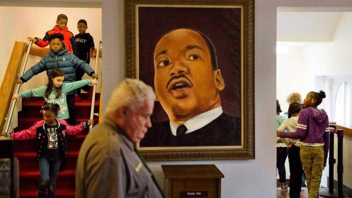 Un retrato del Dr. Martin Luther King Jr. en la Iglesia Bautista Ebenezer donde King predicó, mientras niños recorren el edificio histórico durante un evento para celebrar el cumpleaños del ícono de los derechos civiles asesinado en Atlanta, el viernes 12 de enero de 2018.
