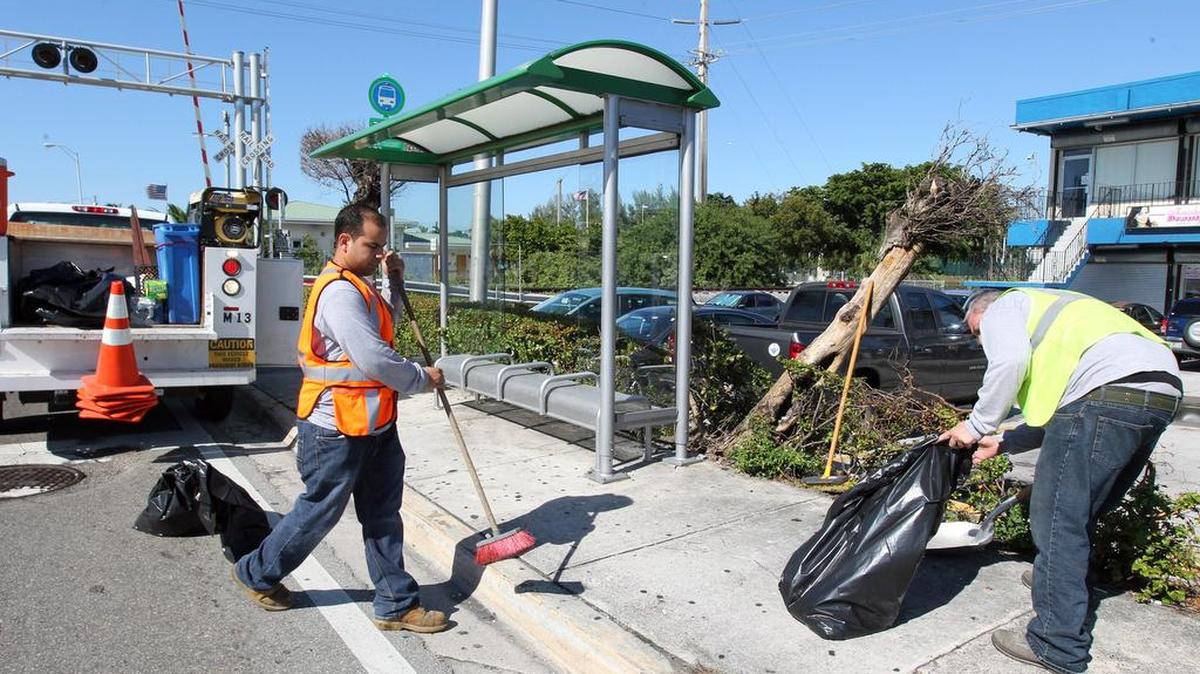 Los empleados Rene Ramos (izq.) y Orlando Exposito limpian los cristales rotos de la parada de Flagler y la 69 Ave, que fue una de las paradas destrozada por vándalos el lunes.