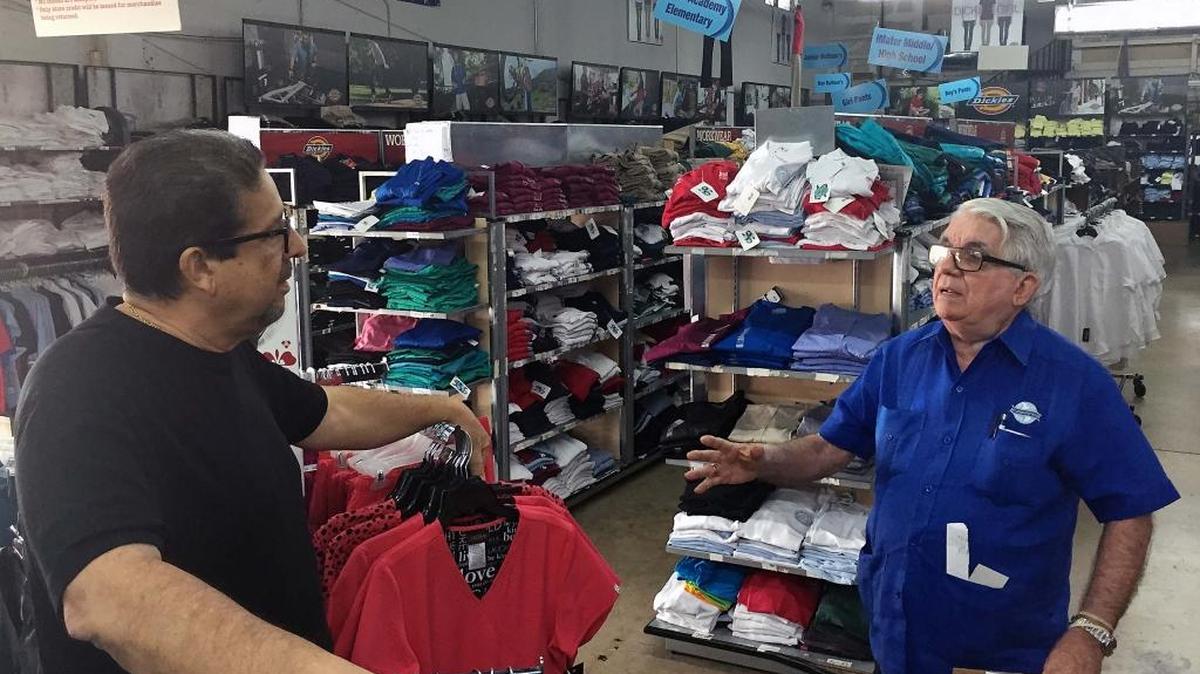 El presidente de la Cámara de Comercio e Industrias de Hialeah, Mandy Llanes, (izq.) conversa con Moisés de Paz, dueño de All Uniform Wear, en la sede central de esa cadena, en Hialeah.