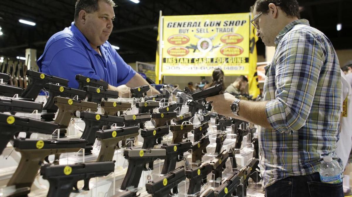 Julio Piloto, dueño del Tienda de armas General, a la izquierda, muestra al cliente Pedro Silva, de Homestead, Fla., una Glock 19 en una feria de armas.
