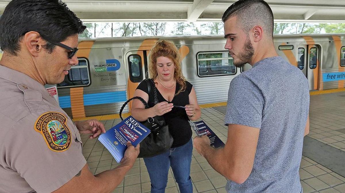 El agente Diego Luna (izq.), de la Policía de Miami-Dade. entrega volantes a pasajeros del Metro Rail en la estación Palmetto en Medley como parte de la campaña “See something - say something” que explica como reportar situaciones o conductas sospechosas.