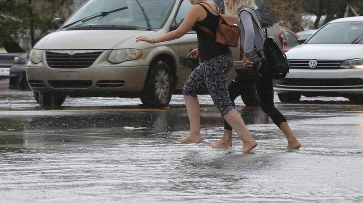 Dos mujeres cruzan la inundada avenida Collins con la calle 24 el jueves en Miami Beach.