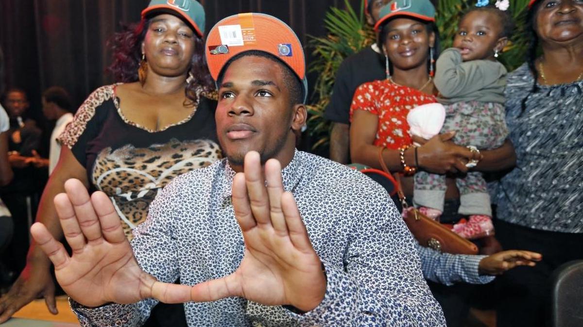 El jugador de la Universidad de Miami, Mark Walton (centro), hace con las manos el símbolo de la universidad luego de ser seleccionado para integrar su equipo, el 4 de febrero del 2015.