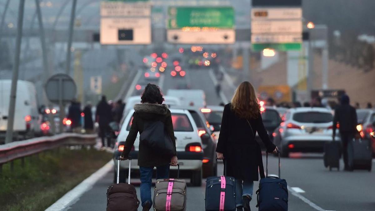 Personas caminan con sus maletas en una carretera hacia el aeropuerto Orly en Francia, debido a una protesta en la zona.