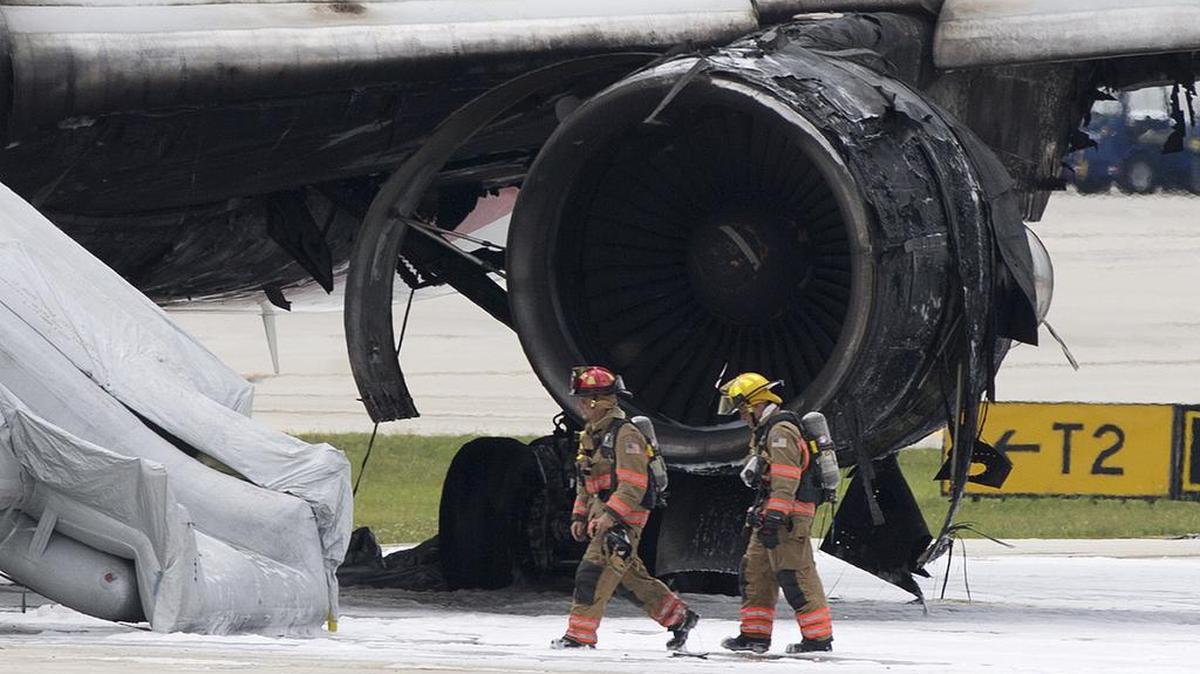 Dos bomberos pasan junto a un avión que se incendió el jueves en el Aeropuerto Internacional Fort Lauderdale-Hollywood.