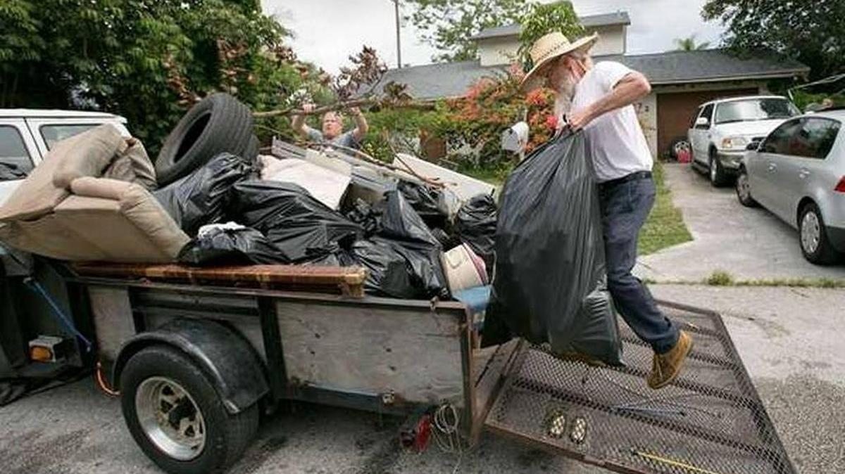 Robert Royall (der.) carga un remolque lleno de basura de la casa de su hijo el sábado pasado. Royall congregó a voluntarios y familiares para ayudar a su hijo, Travis Royall, a limpiar su casa en Lake Worth.