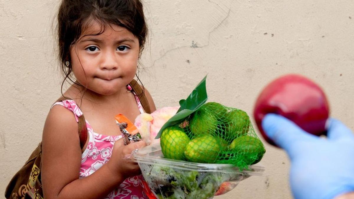 Kasie Pena, de 4 años, recibe una manzana que le ofrece uno de los voluntarios en Glory Temple Ministries en Miami.