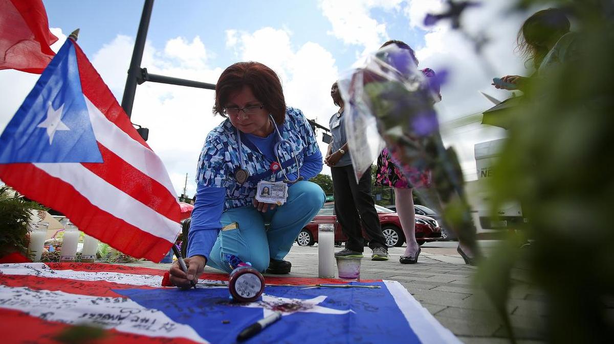 Elizabeth Burgos firma una bandera de Puerto Rico en un sitio en homenaje a las víctimas de la masacre en el club Pulse, afuera de un hospital.