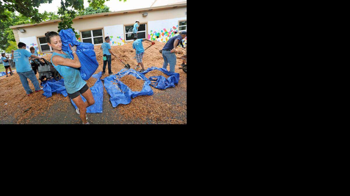 
La voluntaria Courtney Watkins carga una bolsa llena de cubierta vegetal hacia el área de los columpios.


