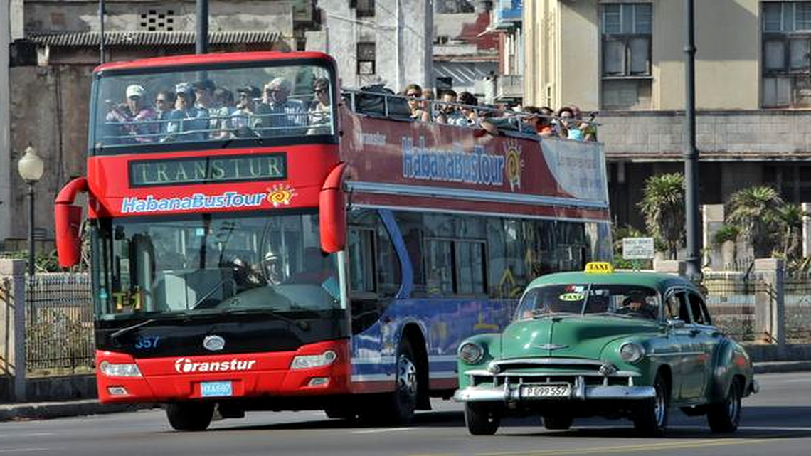 
Un autobús con turistas pasa junto a un taxi de época este domingo 18 de enero en La Habana. 
