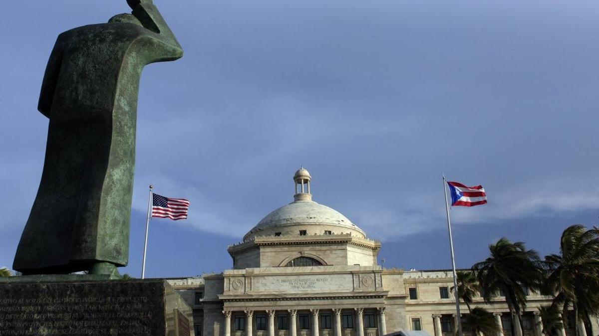 La estatua de San Juan Bautista frente al Capitolio de Puerto Rico flanqueado por las banderas de EEUU y de la isla. Foto de archivo.