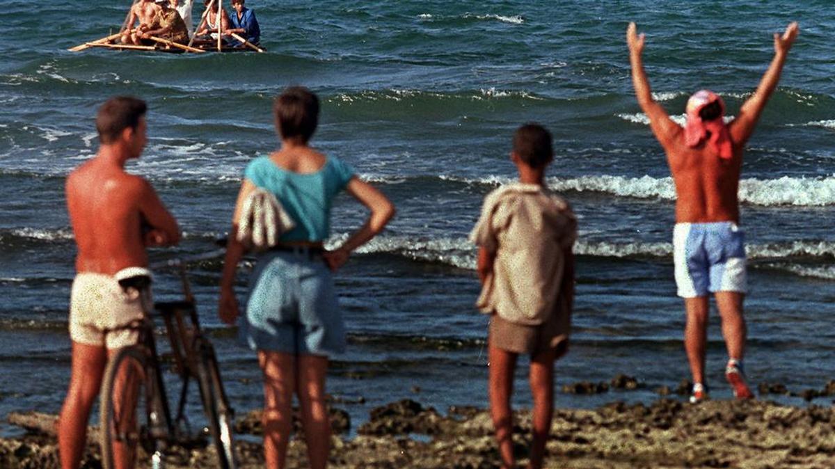 En 1994, los balseros cubanos convirtieron al pequeño pueblo pesquero de Cojimar en un importante punto de embarque para miles de personas que buscaban una vida mejor. Aquí, balseros cubanos parten de la costa de Cojímar mientras los espectadores observan desde la playa rocosa.