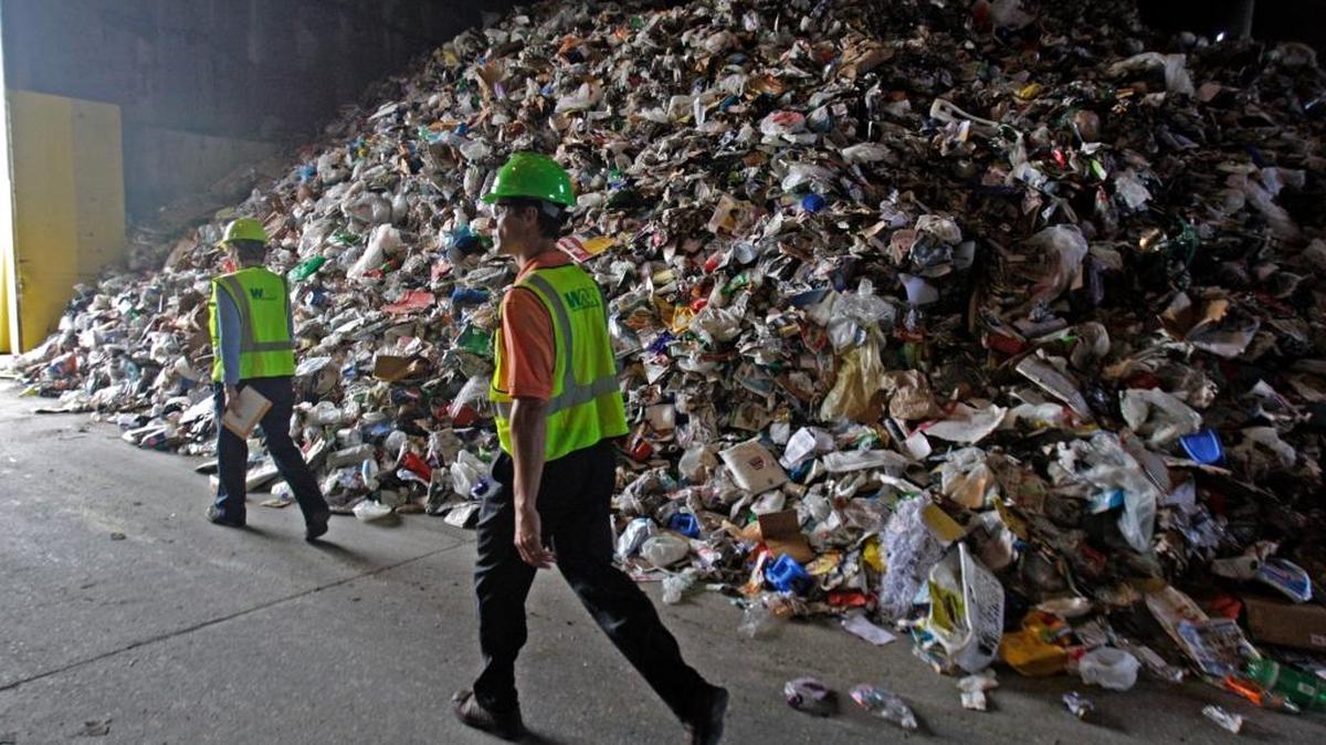 Empleados de Waste Management, una de las plantas de reciclaje más grandes del país, junto a una montaña de materiales para reciclar.