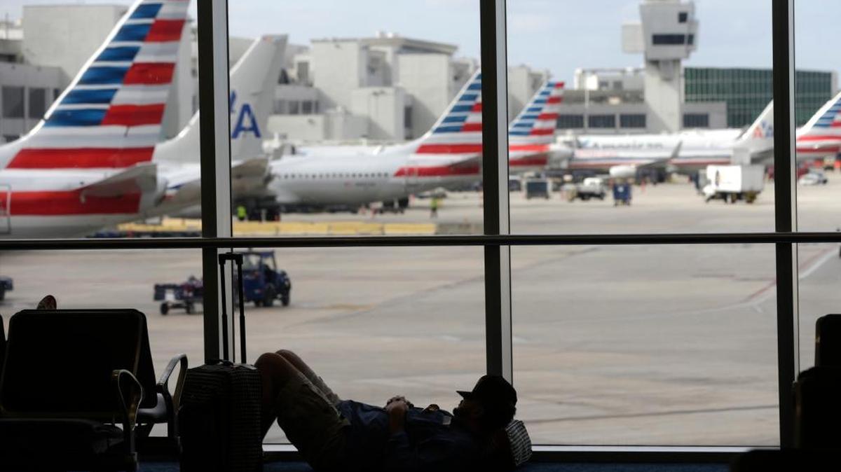 Un viajero descansa en el suelo del aeropuerto de Miami. Al fondo los aviones de AA se aprestan para recibir pasajeros el jueves.