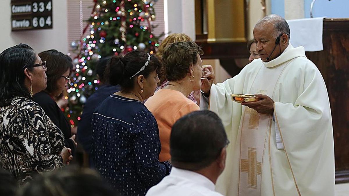 El padre Rafael Cos administra la comunión a un grupo de feligreses que asisten a la misa de Navidad en la Misión Santa ana de Homestead.