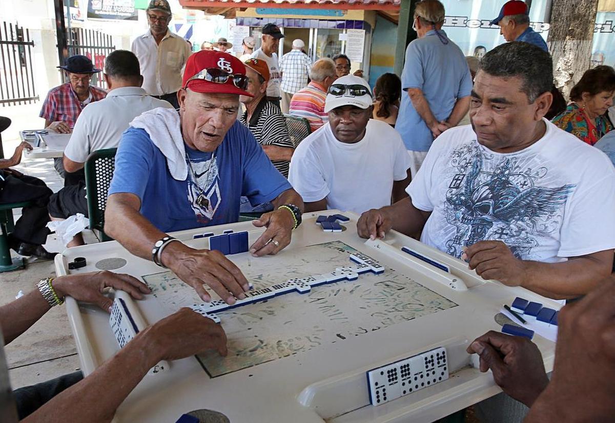 Alfredo Coffiñi, “Pinocho”, a la izquierda, y Roberto García, derecha, en la mesa de juego en el Parque del Dominó de La Pequeña Habana en junio pasado. Entre ambos, Wilfredo Clemente observa la partida. 
