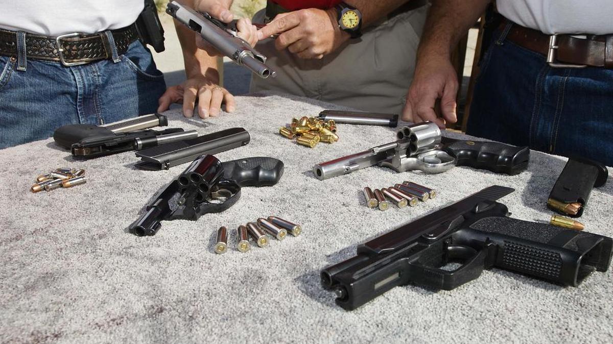 Tres hombres observan armas y municiones en una mesa.
