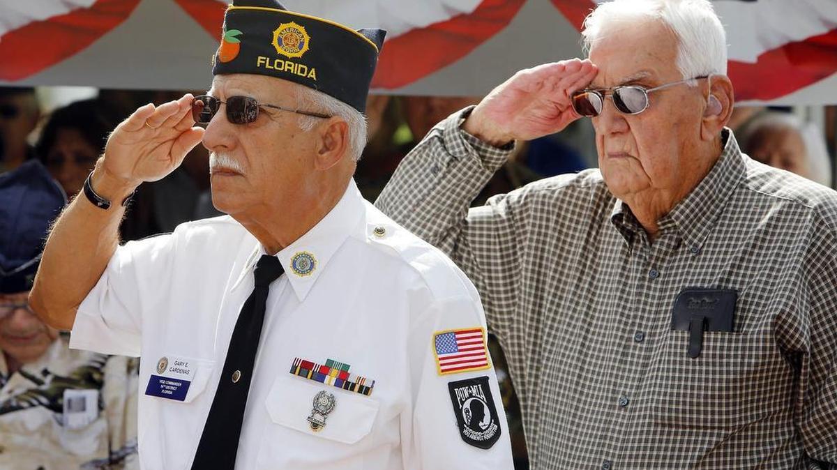 Gary E. Cárdenas, comandante de America Legion Post 144, y Gilbert A. Irizarry (der.), un veterano de la Segunda Guerra Mundial, saludan mientras tocan el himno nacional en la ceremonia del Día de los Veteranos en el Triangle Park de Hialeah.