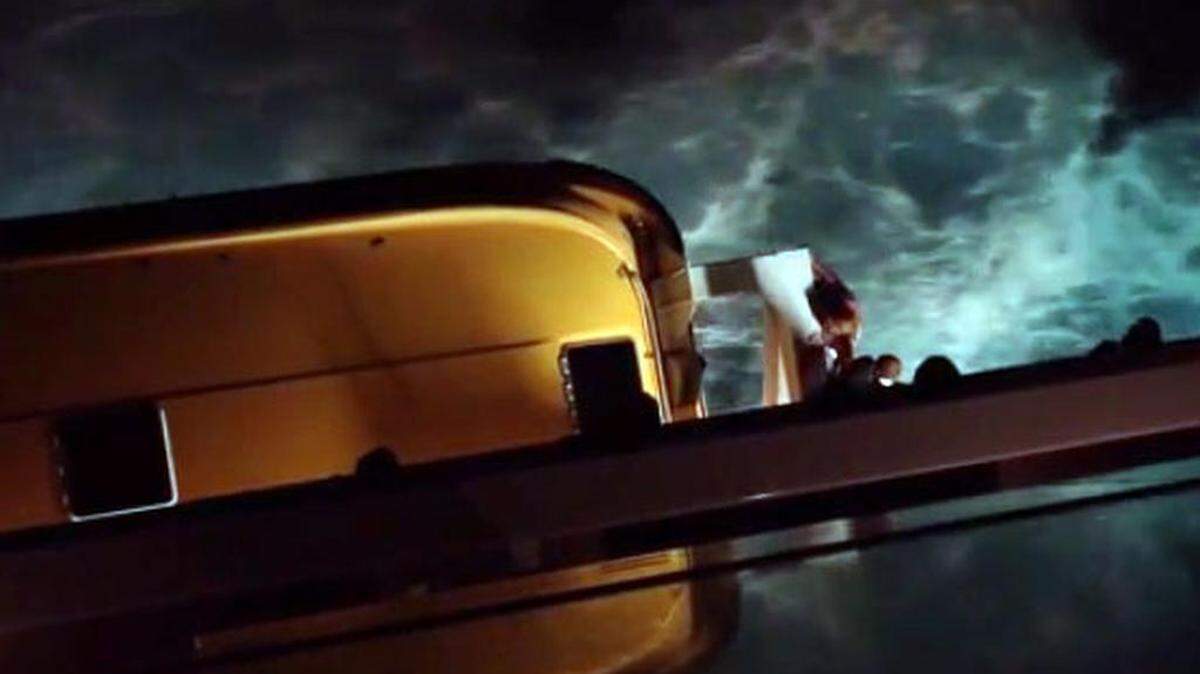 En la imagen tomada del video se puede ver al hombre colgando del barco salvavidas del crucero.