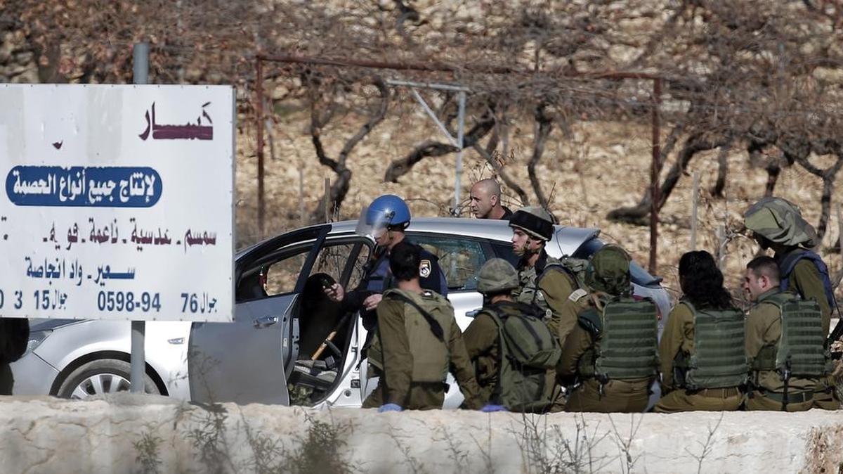 Soldados israelíes investigan el auto que un palestino intentó estrellar contra un retén de seguridad, el viernes cerca de Hebrón, Cisjordania.