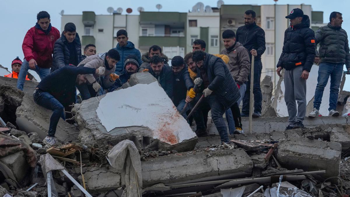 Un grupo de personas busca entre los escombros de un edificio a sobrevivientes tras un sismo, en Adana, Turquía, el lunes 6 de febrero de 2023. (AP Foto/Khalil Hamra)