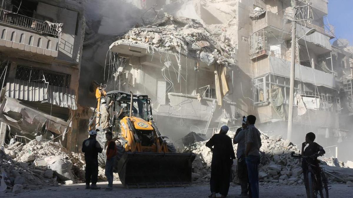 Civiles sirios observan la retirada de escombros de edificios destruidos por bombardeos aéreos realizados por las fuerzas del gobierno, en Alepo.