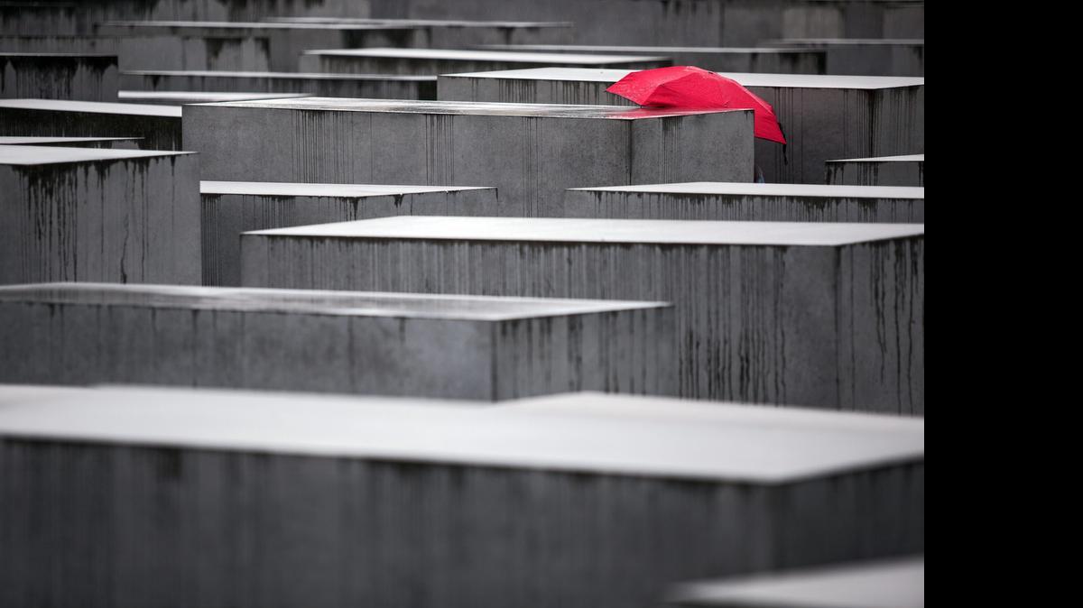 Una persona camina con una sombrilla roja entre el memorial del Holocausto en Berlín (Alemania).