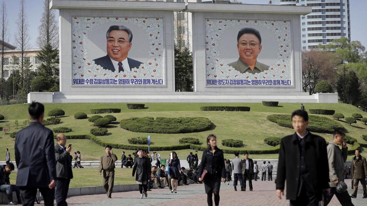 Foto del 18 de abril de 2017 muestra a gente caminando bajo los retratos de Kim Il Sung, Kim Jong Il y Kim Jong Il, en Pyongyang, Corea del Norte.