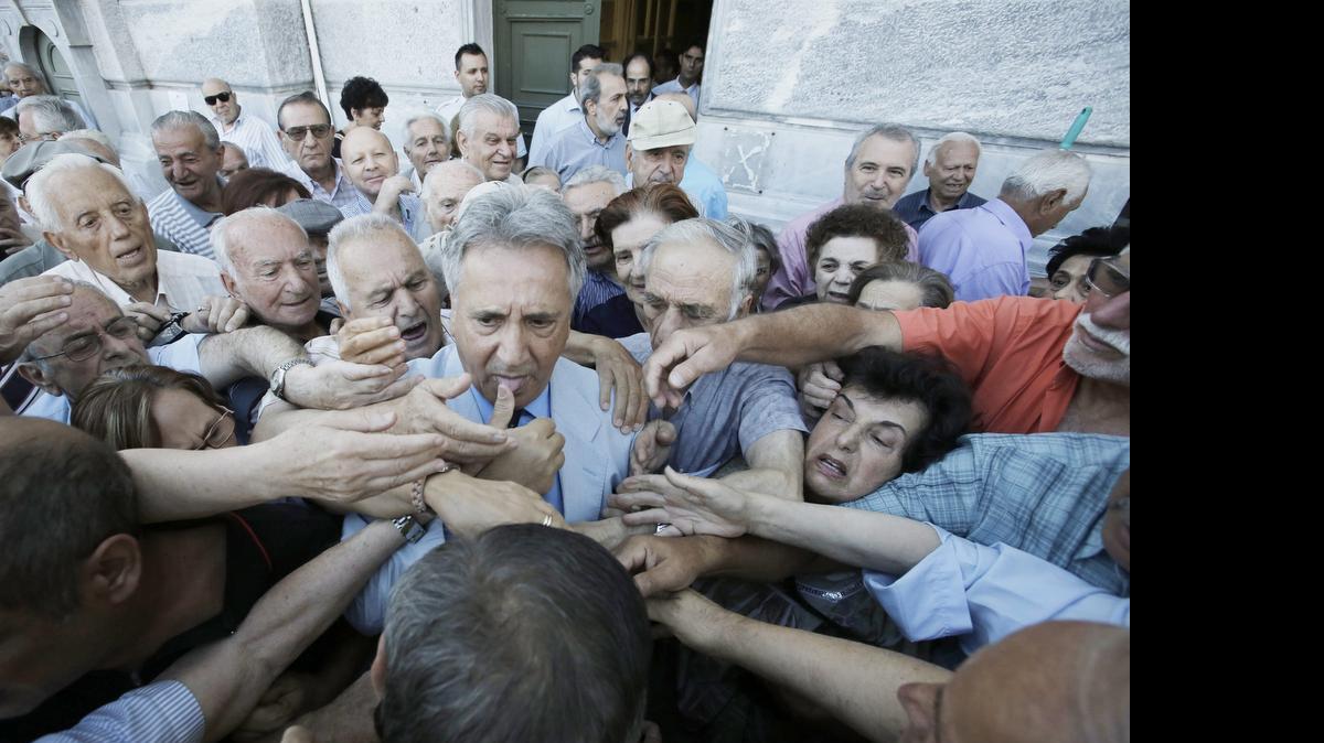
Un empleado del Banco Nacional de Grecia (c) es asediado el miércoles por un grupo de pensionistas mientras distribuye números para ser atendidos a las puertas de una sucursal bancaria en Atenas.
