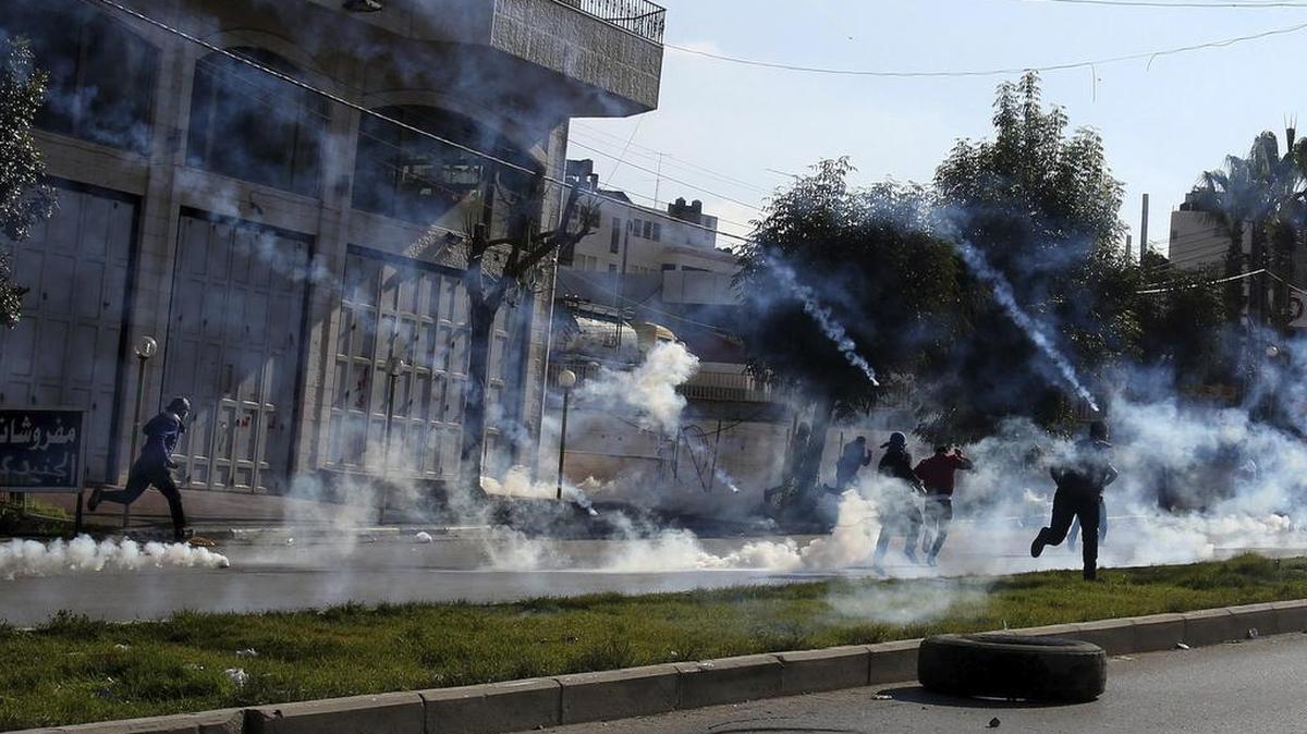 Manifestantes palestinos corren para protegerse de los gases lacrimógenos lanzados por soldados israelíes.