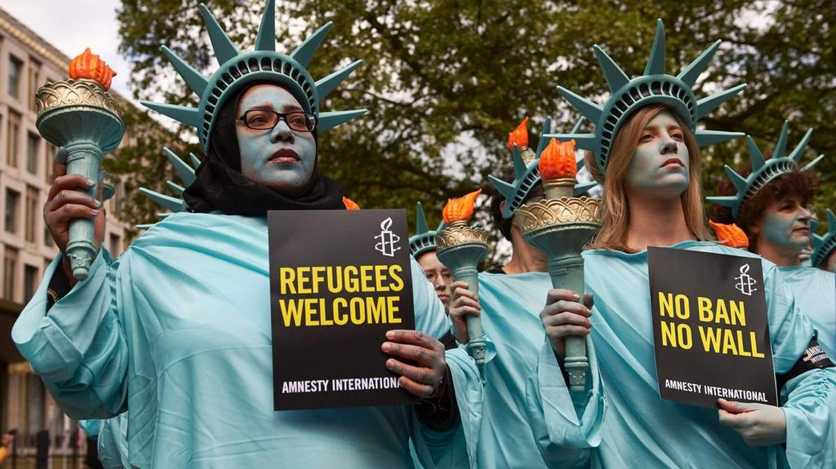 Activistas de Amnistía, vestidos como Estatua de la Libertad, participan en una manifestación por los primeros 100 días de mandato del Presidente de los Estados Unidos, Donald Trump, frente a la Embajada de Estados Unidos en Londres el 27 de abril de 2017.