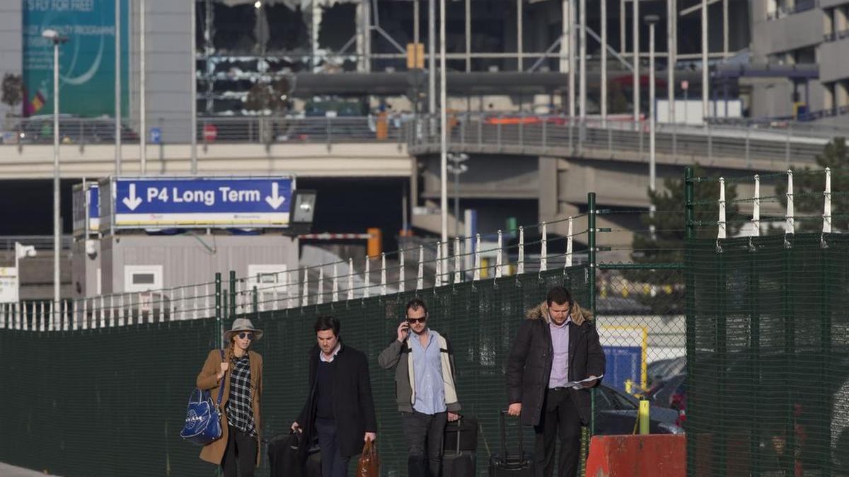 Varias pasajeros abandonan el aeropuerto de Bruselas, que se ve al fondo con las ventanas destruidas por los ataques terroristas el martes 22 de marzo.