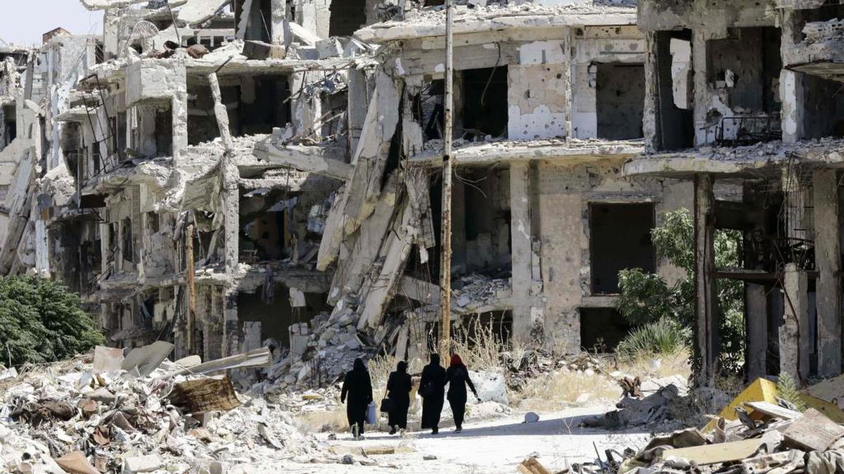 Mujeres caminan entre edificios destruidos en el sector de Jouret al-Shiah, un barrio controlado por el gobierno sirio, en la ciudad de Homs, Siria, el lunes 19 de septiembre.