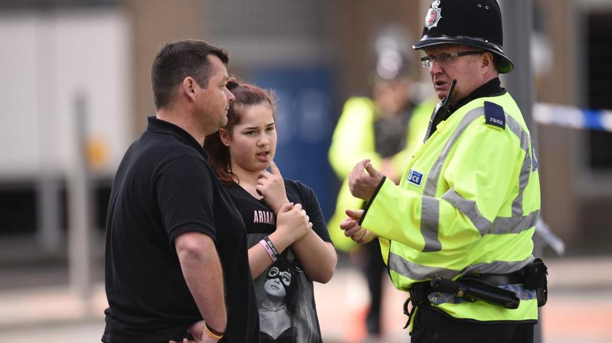 Un oficial de policía habla con un hombre y una niña con una camiseta de la cantante estadounidense Ariana Grande tras un mortal ataque terrorista en el concierto en Mánchester.