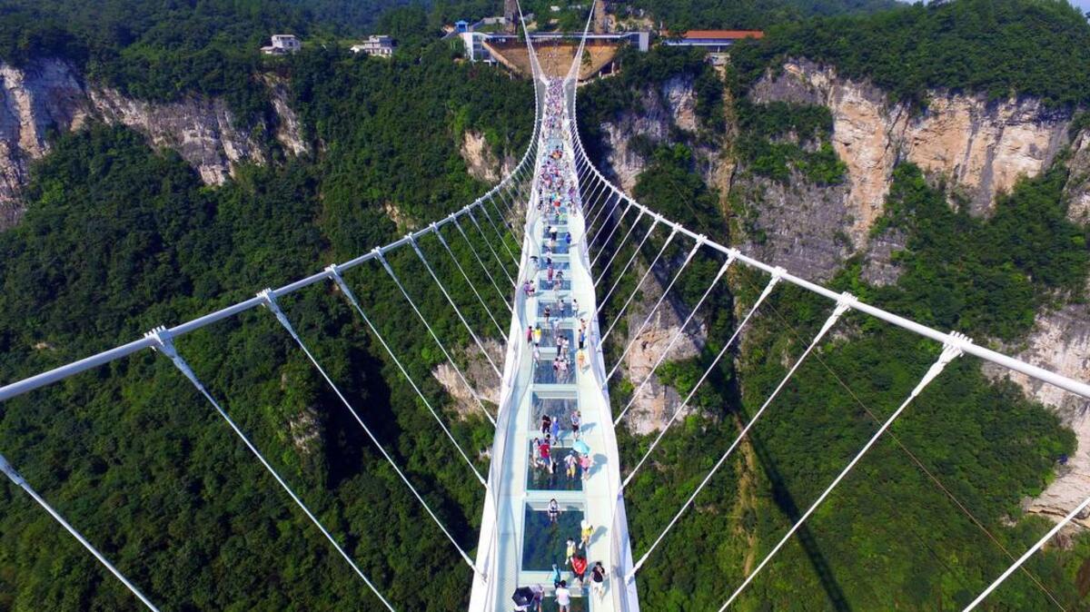 Visitantes caminan a través de un puente colgante de cristal en Zhangjiajie en la provincia de Hunan, sur de China el sábado, 20 de agosto de 2016. El puente se extiende por 430 metros (1,410 pies) y se eleva a unos 300 metros (984 pies) sobre un valle en una zona escénica.