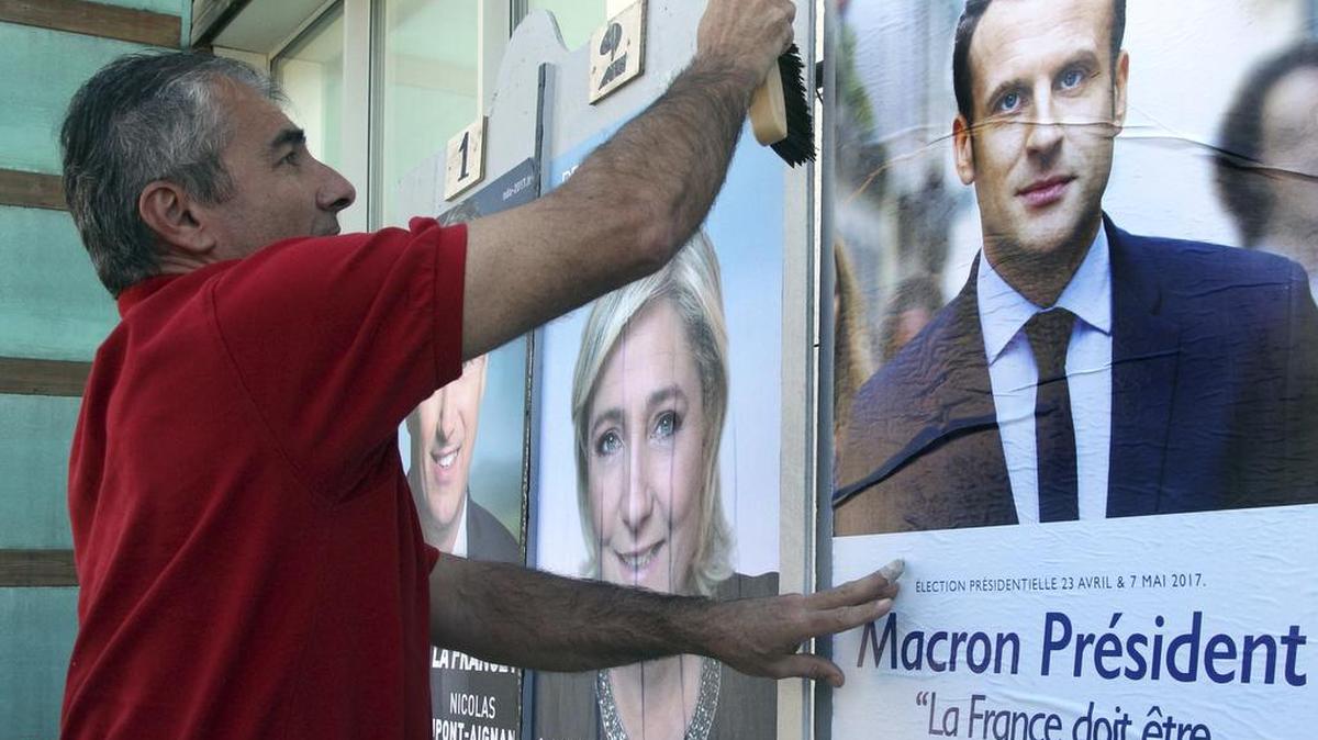 Christophe Sanz, un simpatizante del candidato centrista Emmanuel Macron, coloca un afiche al lado de una imagen de la candidata de extrema derecha Marine le Pen, en Bayonne, en el suroeste de Francia, el 19 de abril de 2017.