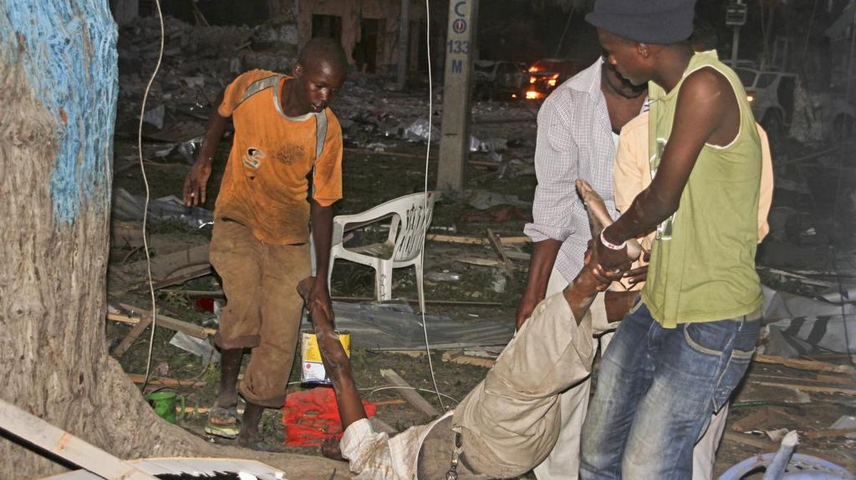 Tres hombres retiran el cadáver de un civil que falleció en el ataque terrorista el Hotel Ambassador de la capital somalí el miércoles.